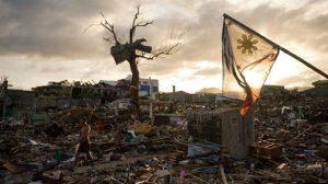 A-man-walks-along-as-the-national-flag-of-the-Philippines-flies-over-the-rubble-of-destroyed-homes-in-Tacloban-AFP